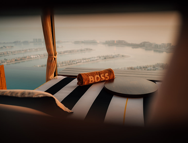HUGO-BOSS towel on a lounger; in the background there are the sea and some buildings (photo)