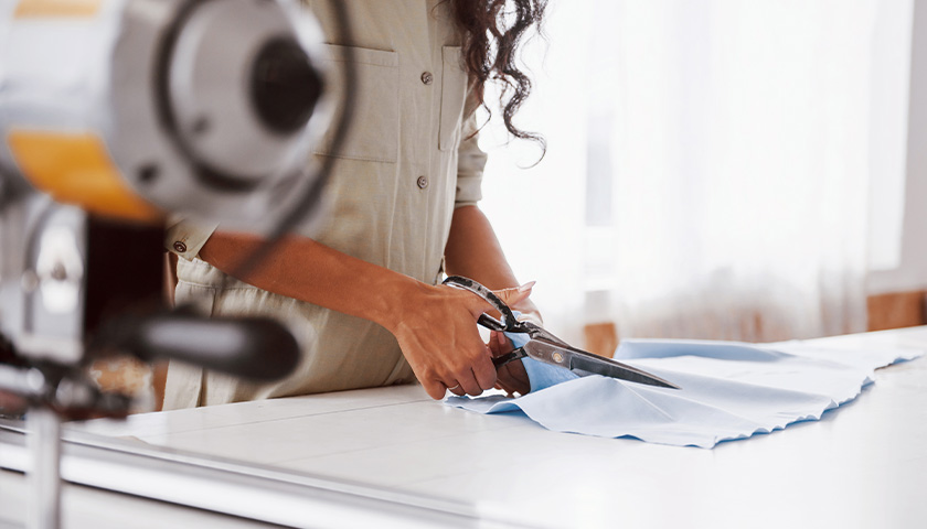 A woman cuts light-blue fabric with scissors (photo)