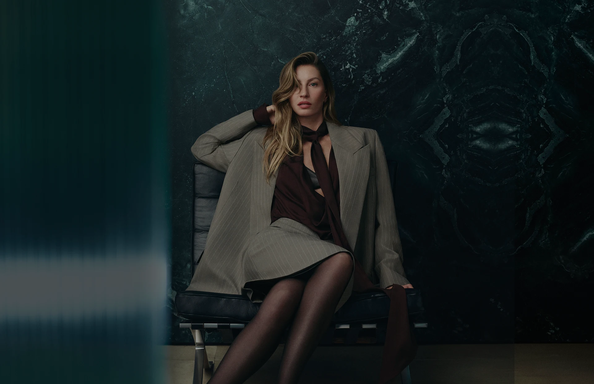 Gisele Bündchen posing in a light-colored women’s suit in front of a dark background (photo)